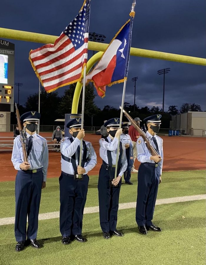 Cadets Hunter Knutson, Victor Tamez, Olivia Garcia and Terrell Wallace holding flags on the football field.  
